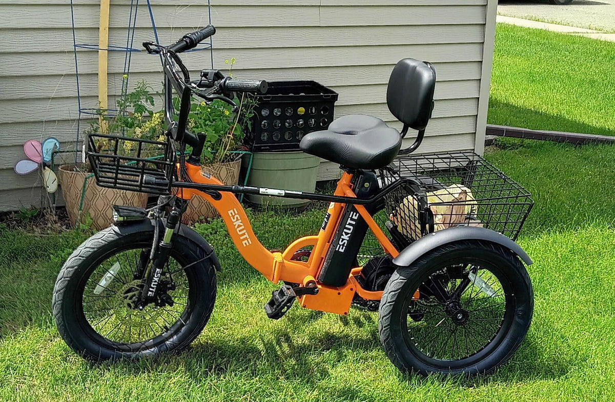 Orange Eskute T300Max electric trike with front and rear baskets and a padded backrest seat, parked on grass.