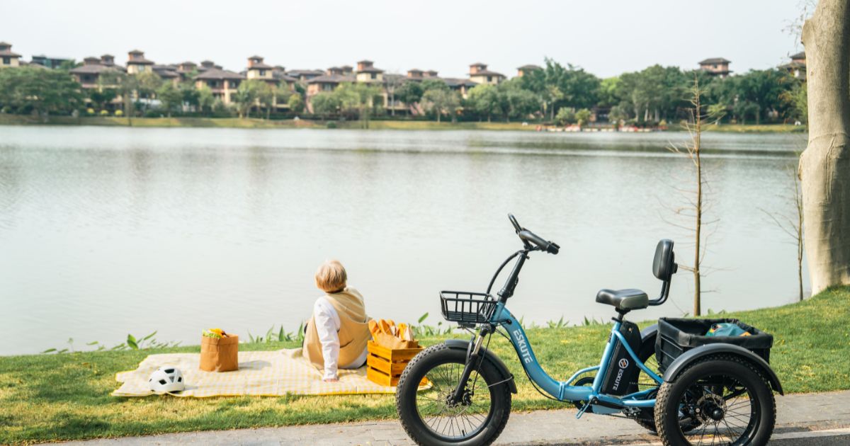 A peaceful scene of a person sitting on a picnic blanket by a lake with a blue electric tricycle parked nearby